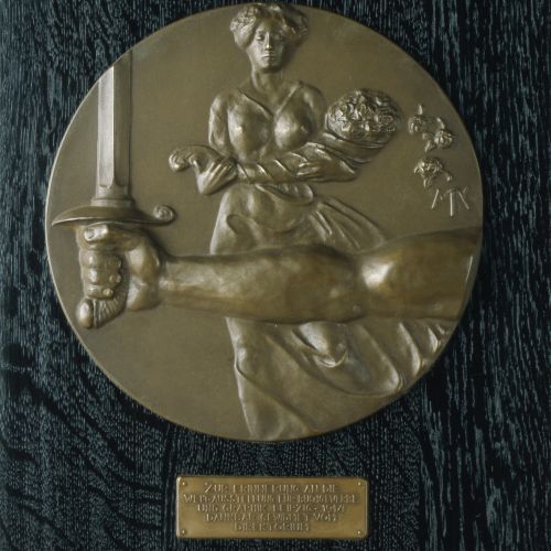 Es handelt sich um eine Medaille von Max Klinger, die der Künstler im Jahr 1914 zur Erinnerung und zu Ehren der Weltausstellung für Buchgewerbe und Graphik, die durch den ersten Weltkrieg unterbrochen wurde, angefertigt hat