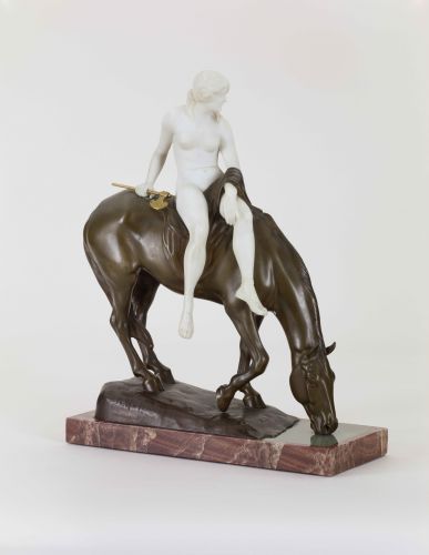 Eine Kleinplastik aus Bronze zeigt eine Amazone, seitlich auf dem Rücken eines trinkenden Pferdes sitzend