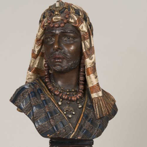 Die polychrom gefasste Plastik von Rudolf Uffrecht stellt das Brustbild eines bärtigen Orientalen mit reichem Kopf- und Halsschmuck in gestreiftem Gewand dar.